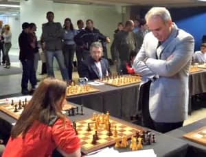 Garry Kasparov de pé diante do tabuleiro em que Thauane Medeiros joga, durante a simultânea