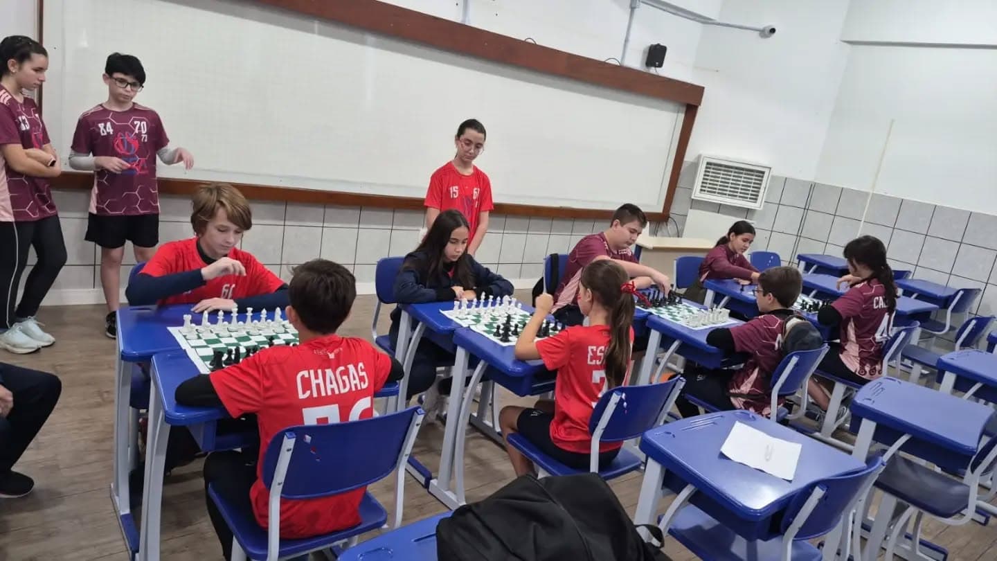 Turma de estudantes uniformizados jogando xadrez em duplas, numa sala de aula